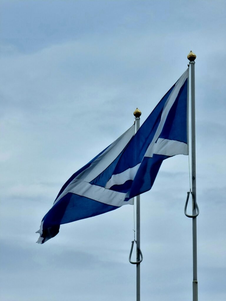 Two Scottish flags wave proudly on poles beneath a blue sky, symbolizing national pride.