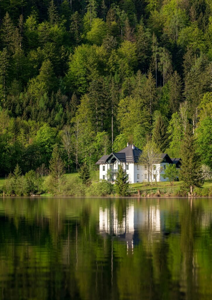 Serene lakeside house surrounded by lush forest in Ebensee, reflecting on calm waters.