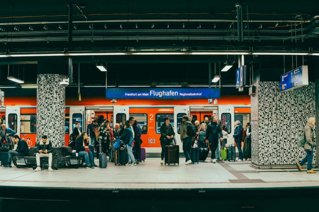 pexels-photo-36023564-36023564 Passengers wait on the platform at Frankfurt am Main Flughafen train station with a regional train in the background.