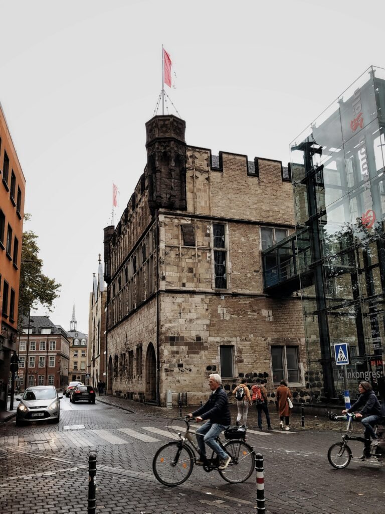 pexels-photo-4803317-4803317-1 Cyclists pass by the medieval Gurzenich building in Cologne, blending history with urban life.